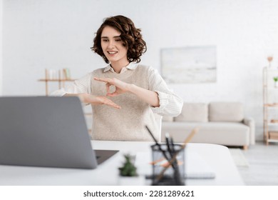 happy teacher with curly hair showing sign language gesture during online lesson on laptop - Shutterstock ID 2281289621