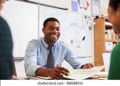 Happy Teacher At Desk Talking To Adult Education Students