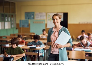 Happy teacher during a class at elementary school looking at camera. Her student are learning in the background. - Shutterstock ID 2183353397