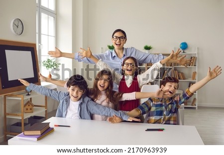 Happy teacher and group of children laughing, shouting hooray and looking at camera. Young woman together with her students having fun excited about start of holiday, summer break or school vacation