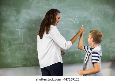 Happy Teacher And School Boy Giving High Five In Classroom At School