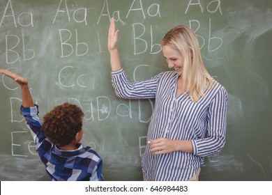 Happy Teacher And Schoolboy Giving High Five In Classroom At School