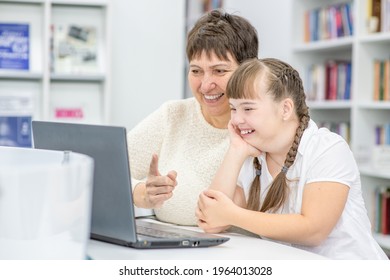 Glücklicher Lehrer und lächelndes Mädchen mit Down-Syndrom benutzen einen Laptop in der Bibliothek. Konzept "Bildung für behinderte Kinder"