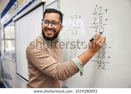 Happy teacher teaching how to do the column additions at elementary school. Smiling man explaining additions in column in primary class while writing on whiteboard. Math’s teacher explaining sums.