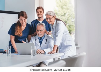 Happy team of healthcare workers having meeting in boardroom while looking in laptop. Teamwork of medical workers. Doctors discussing treatment for patients - Powered by Shutterstock