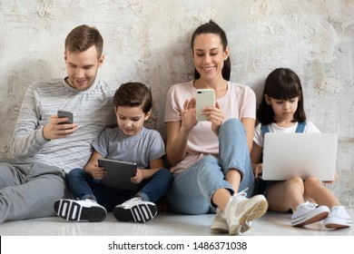 Happy Technology Addicted Family Parents And Kids Use Laptop Phone Digital Tablet Sit On Floor At Home, Mom Dad With Children Obsessed With Devices Overuse Social Media, Internet Addiction Concept