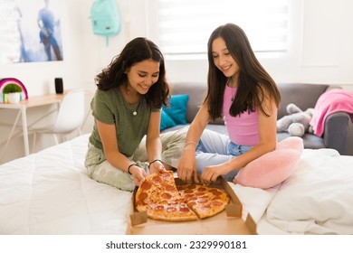 Happy teen best friends smiling looking cheerful and eating pizza while hanging out in the bedroom together - Powered by Shutterstock