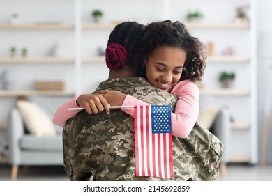 Happy Teen Black Girl With Flag Of The US Hugging Her Mom Wearing Camouflage Uniform, Daughter Resting On Her Mother Shoulder, Woman Coming Back Home From Military Service, Copy Space