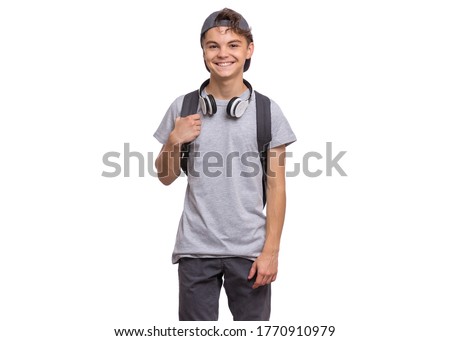 Happy teen boy in cap with headphones and backpack, isolated on white background. Cheerful child smiling and looking at camera. Emotional portrait of handsome teenager guy Back to school.