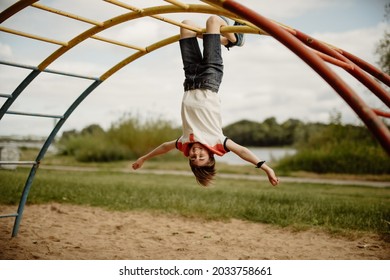 happy teen boy enjoy childhood by hanging upside down from pole of a climbing frame on playground - Powered by Shutterstock