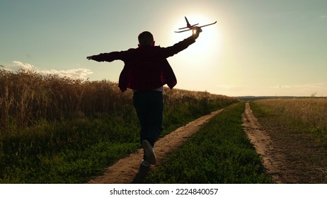 Happy Teen Boy Plays With Toy Plane On Field, Sunset. Boy Wants To Become Pilot Astronaut. Slow Motion. Silhouette, Teenager Dreams Of Flying, Becoming Pilot Airplane. Children Play With Toy Airplane