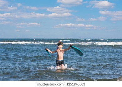 Happy teen boy in the swim flippers and snorkeling mask running оn the wave of the sea during summer vacation in the tropical resort town