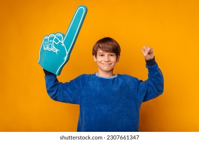 Happy teen boy wearing blue foam finger fan glove makes the winner gesture over yellow background. - Powered by Shutterstock