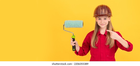 Happy Teen Child In Builder Hard Hat With Paint Roller On Yellow Wall. Pointing Finger. Child Builder In Helmet Horizontal Poster Design. Banner Header, Copy Space.