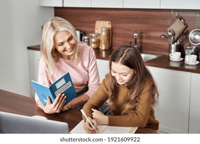 Happy Teen Child Daughter And Mom Learning English Together Studying At Home In Kitchen. Teenage School Kid Girl Distance Learning With Mother, Grandma Or Tutor Helping Doing Homework Remote Education