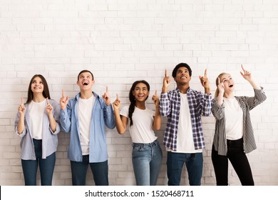 Happy Teen Friends Pointing Up On Free Space Over White Brick Wall, Standng In Row