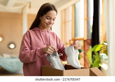 Happy Teen Girl Buyer Holding New Footwear Unpacking Cardboard Box In Bedroom Interior At Home. Young Customer Receiving Shoes After Successful Online Shopping