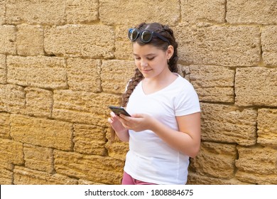 Happy teen girl checking social media holding smartphone over stone wall background