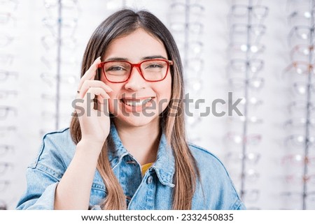 Happy teen girl in eyeglasses on a background of optical store. Happy female customer modeling glasses in an optical store