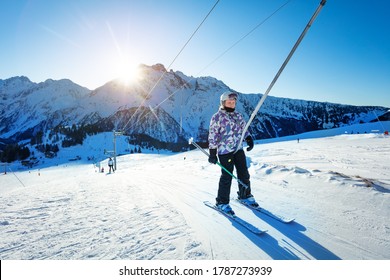 Happy teen girl lifting on the ski drag lift rope in bright sport outfit over sunset light near mountain peak