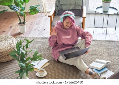 Happy Teen Girl School College Student Pink Hair Wear Headphone Waving Hand Video Conference Calling On Laptop Computer Sit On Floor Distance Learn Zoom Online Virtual Meeting At Home Office. Top View