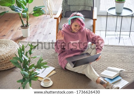 Happy teen girl school college student pink hair wear headphone waving hand video conference calling on laptop computer sit on floor distance learn zoom online virtual meeting at home office. Top view