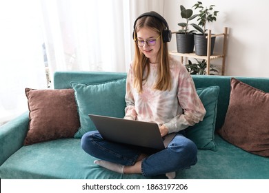 Happy teen girl wear headphones sit on sofa at home video calling on laptop. Video chat concept - Powered by Shutterstock