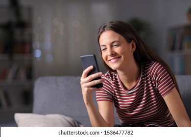 Happy Teen In The Night Using Mobile Phone Sitting On A Couch In The Night At Home