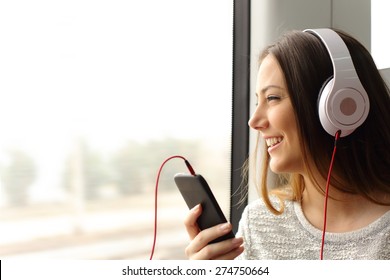 Happy teen passenger listening to the music traveling in a train and looking through the window