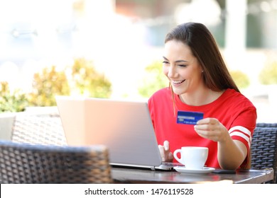 Happy Teen Paying Online Using A Laptop And Credit Card Sitting In A Coffee Shop Terrace