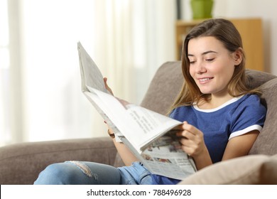 Happy Teen Reading A Newspaper Sitting On A Sofa In The Living Room At Home