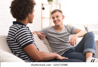 Happy Teen Roommates Talking While Relaxing On Couch At Home