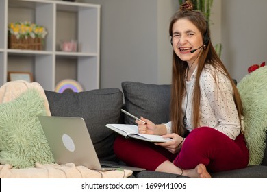 Happy Teen School Student Conference Calling On Computer For Online Distance Learning Communicating With Friend By Webcam At Home. Teenage Girl Wearing Headphones Using Laptop Sitting On Bed.