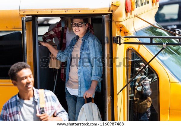happy teen schoolboy walking out of school bus\
with classmates