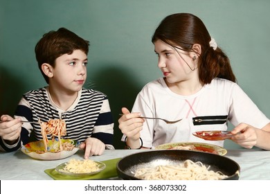 happy teen  siblings boy and girl eat spaghetti together hanging from mouth grimacing happily