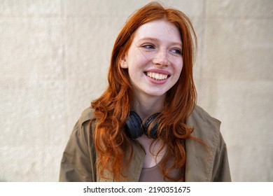 Happy teen stylish cool redhead fashion girl model standing on urban wall background laughing. Close up portrait of pretty joyful smiling teenage hipster girl with red hair looking away outdoors.