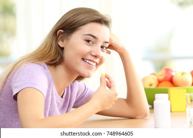 Happy Teen Taking Omega 3 Vitamin Pill On A Table At Home With A Colorful Background