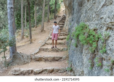 Happy Teen Walking In Woods. A Smiling Black Hair Teenager Wearing A Shorts And T-shirt Walking Down Stone Old Stairs In The Forest.