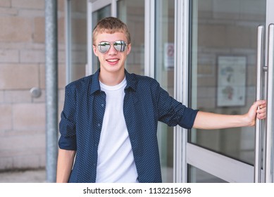 Happy Teen Wearing Sunglasses And Opening A Glass Door To A Building.