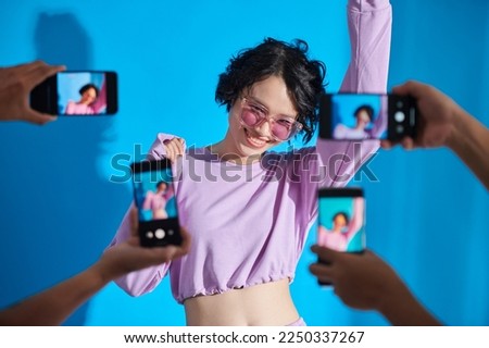 Happy teenage blogger posing when subscribers photographing her on smartphones