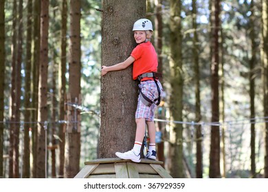 Happy Teenage Boy Climbing On The Ropes In Adventure Park. Healthy Child Enjoying Outdoors Teambuilding Activity On A Summer Day.