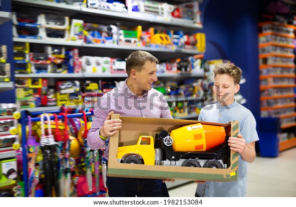 Happy teenage boy with his father buying\
toy cement mixer machine in modern toy\
store