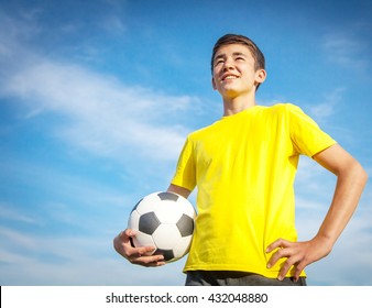 happy teenage boy with a soccer ball on a background of blue sky