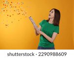 Happy teenage girl blowing up party popper on orange background