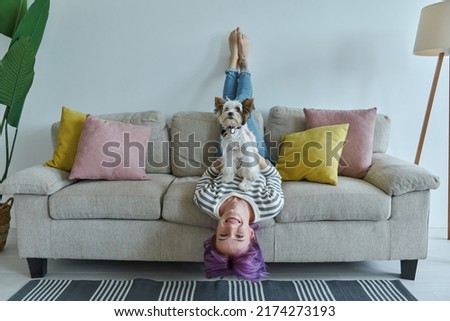 Happy teenage girl carrying her little dog while relaxing on the couch at home