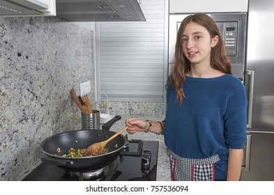 A happy teenage girl cooking a vegan food in a design kitchen.
