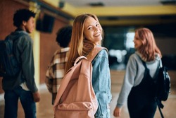 Happy Teenage Girl In Hallway At High School Looking At Camera. Her Friends Are In The Background. 