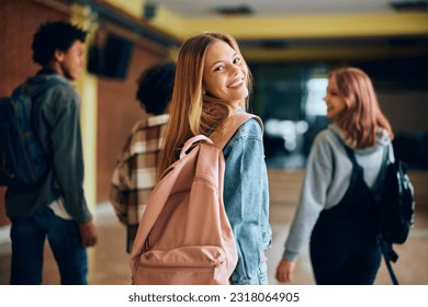 Happy teenage girl in hallway at high school looking at camera. Her friends are in the background.  - Shutterstock ID 2318064905