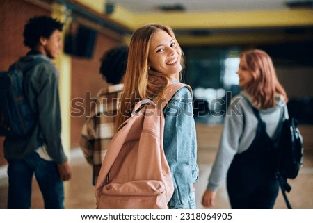 Happy teenage girl in hallway at high school looking at camera. Her friends are in the background. 