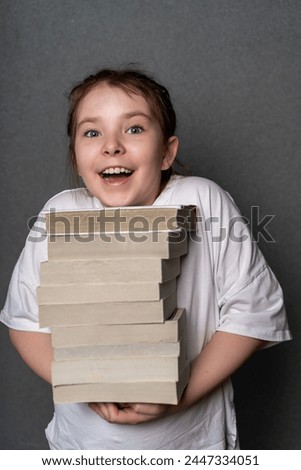 Happy teenage girl holding a big stack of books. Concept of knowledge with pleasure. High quality photo